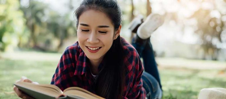 Smiling woman reading a book outdoors representing the question what is a diploma in an academic context