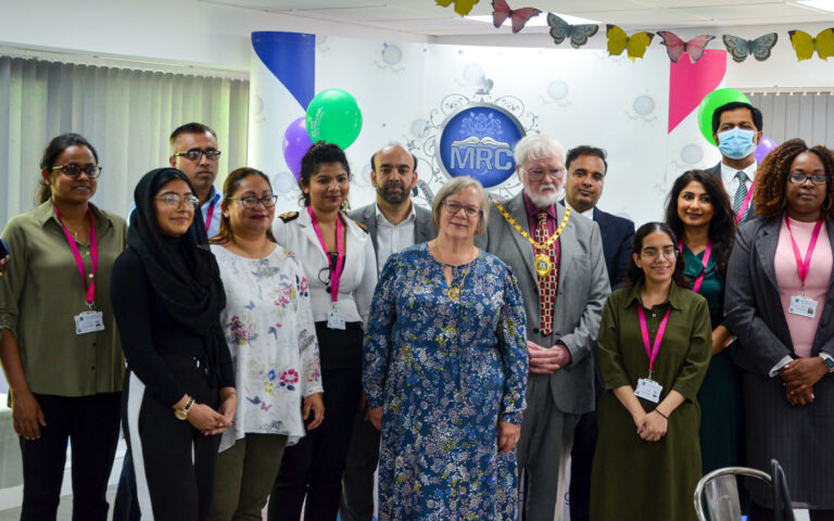 Group of diverse staff smiling at indoor event with decorations, representing community engagement during Coffee Morning.