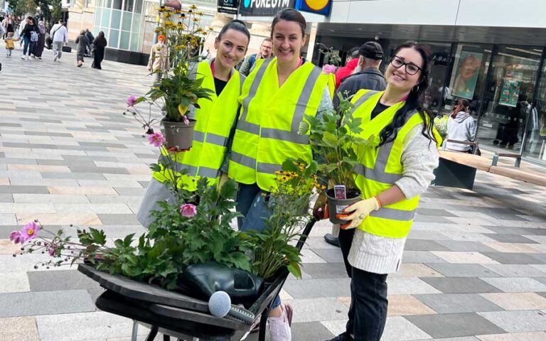 Volunteers in high-visibility vests holding plants on city street, promoting sustainability during Great Big Green Week.