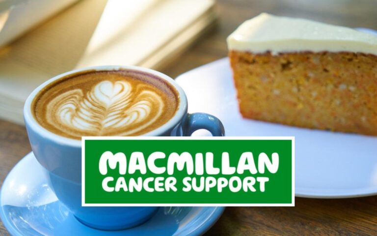 Cup of coffee with latte art and slice of cake beside Macmillan Cancer Support sign, promoting Macmillan Coffee Morning.