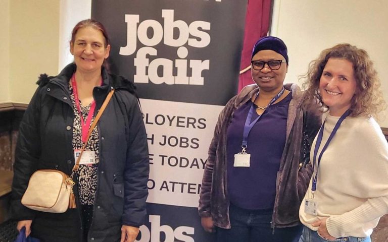Three attendees posing in front of a banner at the Stratford Town Hall Jobs Fair.