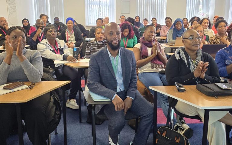 A diverse group of attendees in a classroom enthusiastically clapping during the Anthony Lindsay Black History Month Event at MRCollege.