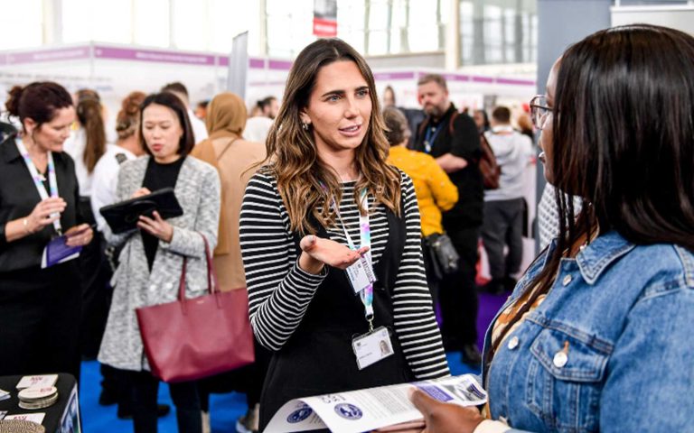 Two women conversing during the Stepping Into Opportunity – London Job Fair at Westfield Stratford, surrounded by attendees and booths.