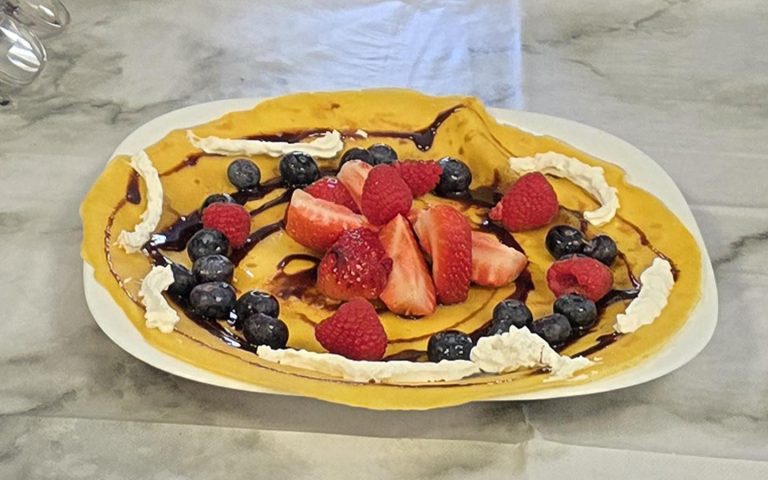 A delicious pancake decorated with strawberries, raspberries, blueberries, whipped cream, and chocolate drizzle for Pancake Day celebrations.