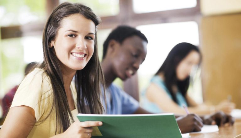 Smiling student holding a green folder in a classroom, representing confidence and success through an HND program.