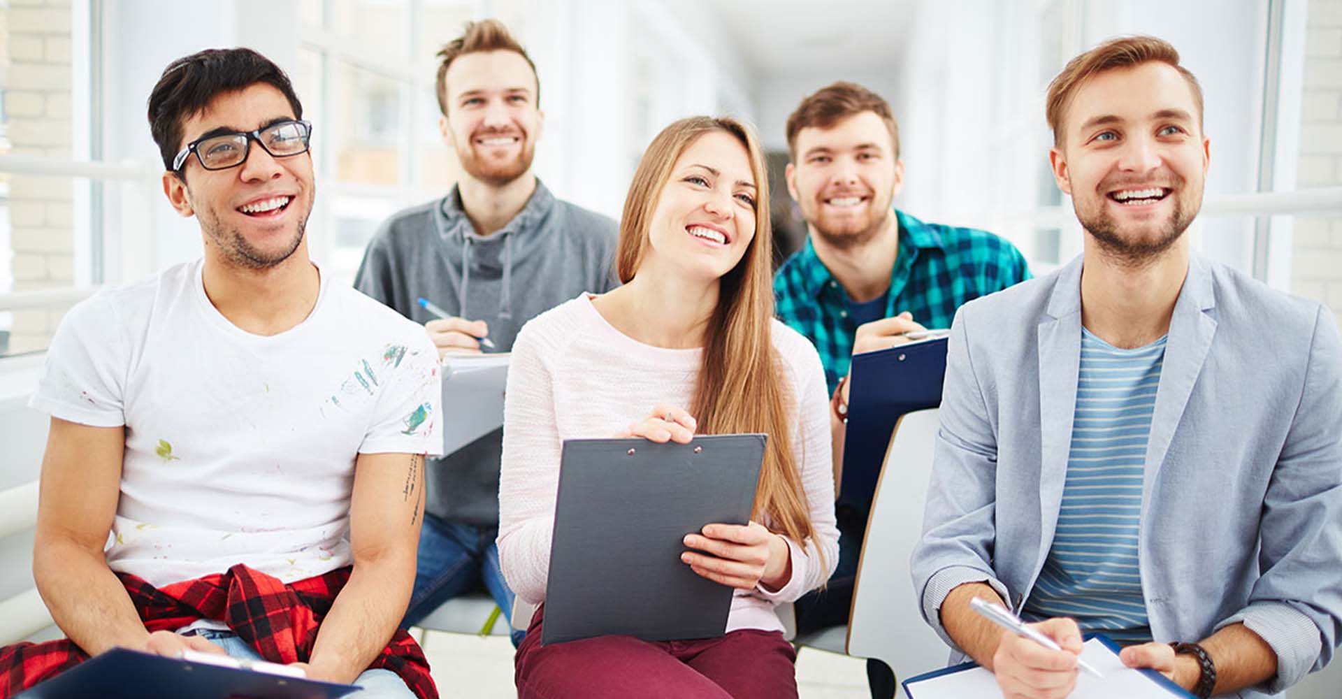 Smiling students holding clipboards in a classroom, representing flexible learning options like HND and Short Courses.