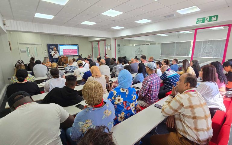 Audience attending a presentation by Matt Whittingham at Mont Rose College, with a slideshow displayed at the front.