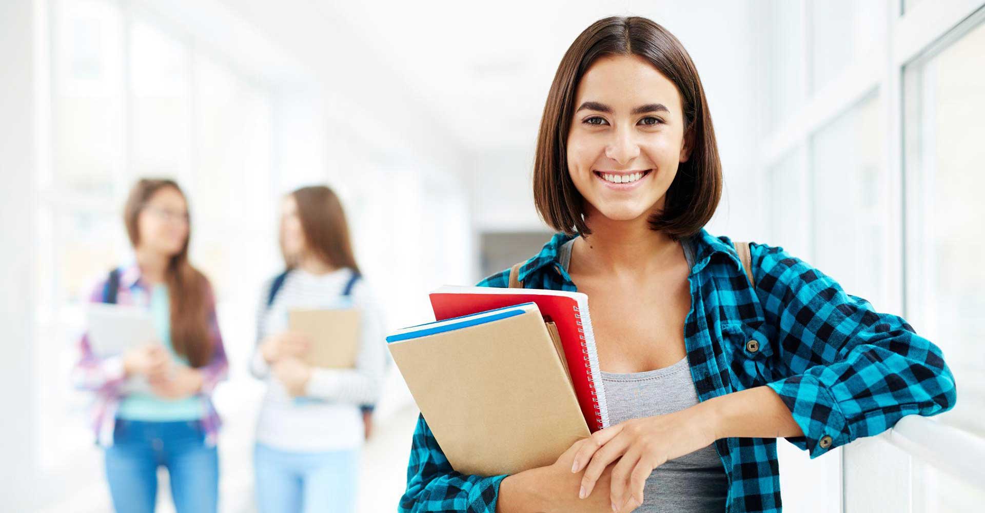 Smiling student holding notebooks in a hallway, symbolizing academic choices in the HND vs HNC pathway.