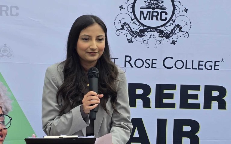 Woman speaking into a microphone at Mont Rose College Careers Fair 2025, standing in front of event banner.