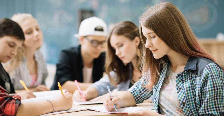 Students attentively filling out forms and writing in notebooks in a classroom setting, representing the HND application process.
