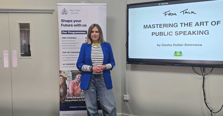 Dasha Dollar-Smirnova standing beside screen at Mont Rose College Public Speaking Workshop presentation.