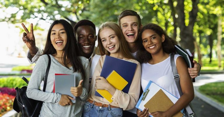 Group of smiling students holding notebooks outdoors representing choices between HND vs Bachelors degree pathways