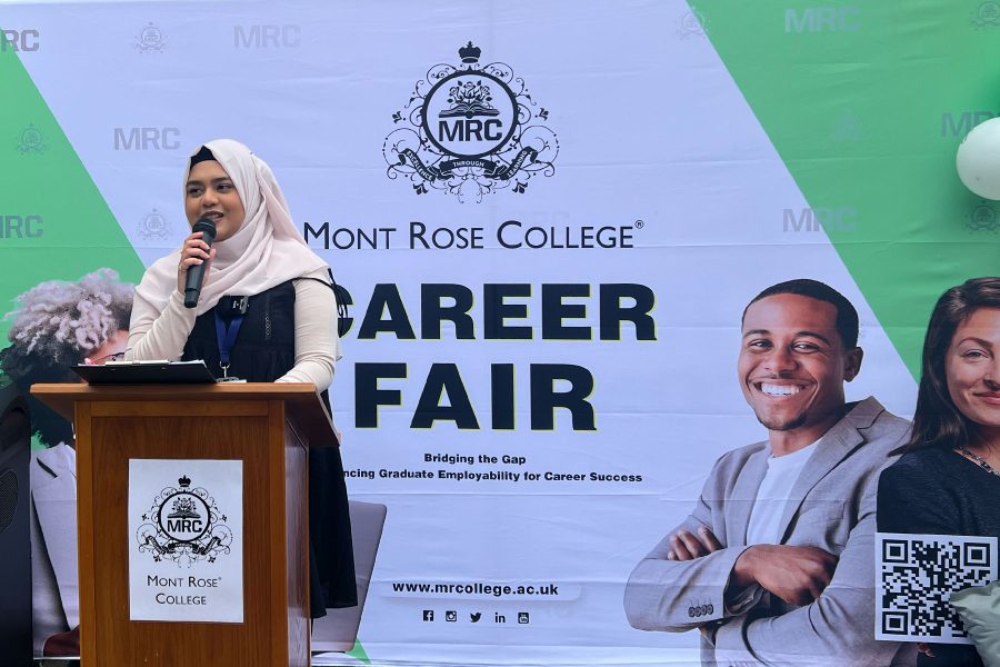 Woman speaking at podium in front of Mont Rose College banner, presenting at Career Fair 2025