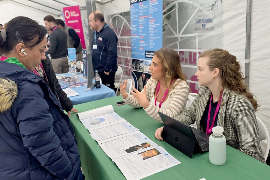 Two representatives discussing opportunities with visitor at booth, sharing information and guidance during Career Fair 2025