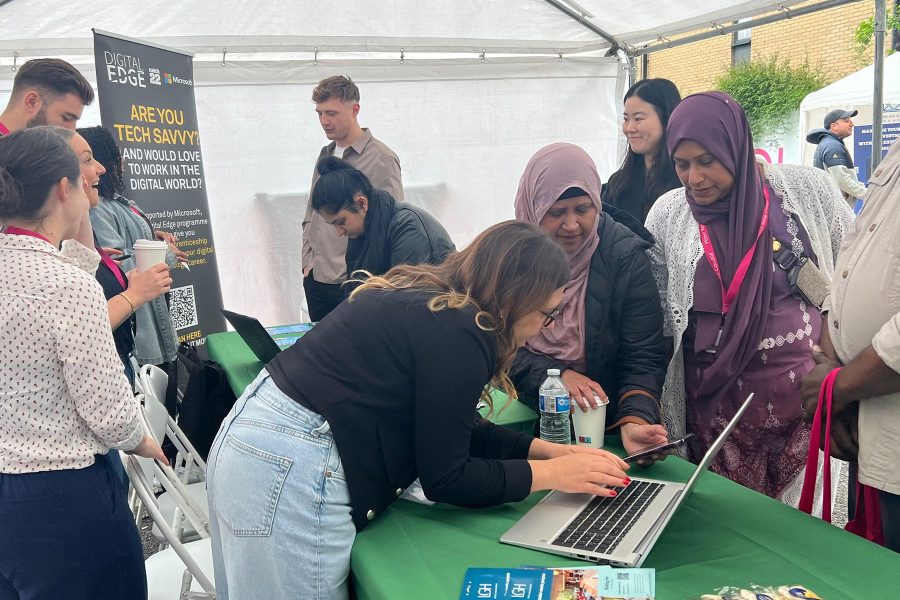 Visitors interacting at tech booth with laptop demonstration, exploring digital skills and opportunities at Career Fair 2025