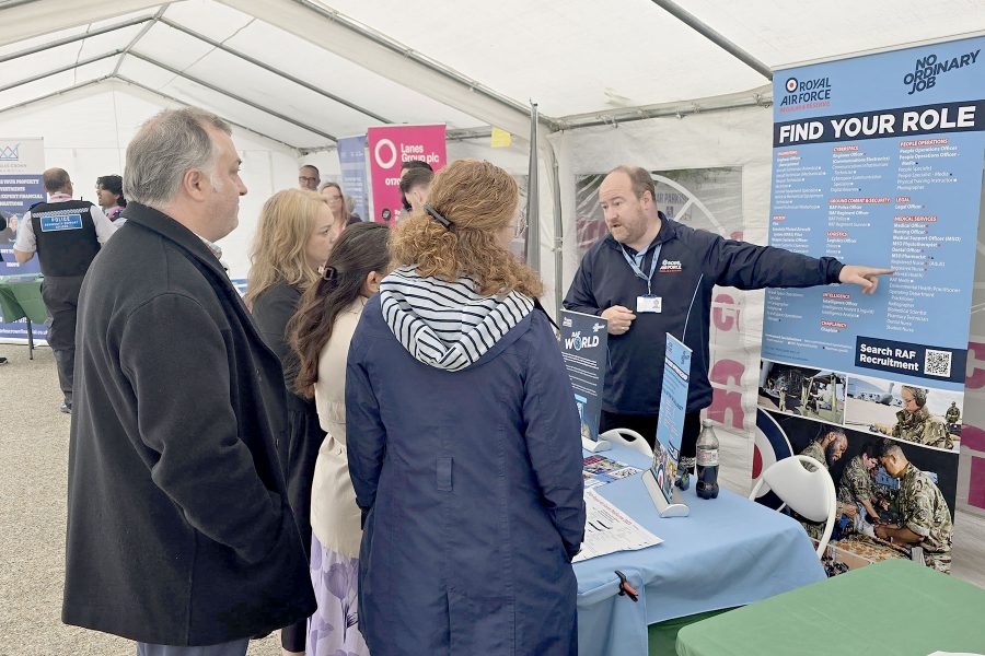 Visitors speaking with exhibitor at information booth inside event tent, exploring opportunities at Career Fair 2025
