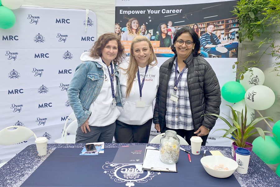 Three staff members smiling at Mont Rose College booth with promotional materials, engaging visitors at Career Fair 2025