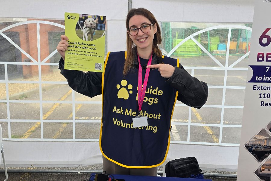 Volunteer holding Guide Dogs poster and smiling at event booth, promoting community engagement at Career Fair 2025