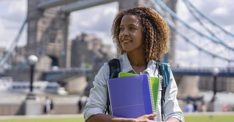 Student holding books near Tower Bridge in London, enjoying vibrant Student Life in Ilford