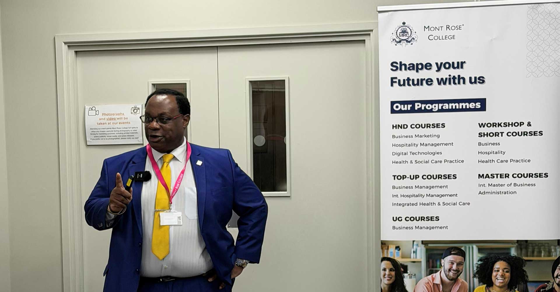 Speaker delivering a presentation on cybersecurity threats and protection strategies beside a Mont Rose College programme banner.