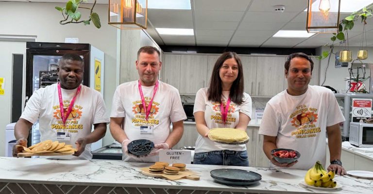 Staff holding pancakes and toppings in kitchen celebrating Pancake Day Mont Rose College event with smiles and food display