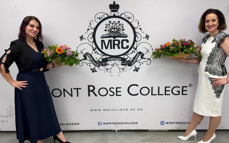 Two women holding flower arrangements and celebrating International Women’s Day 2026 in front of the Mont Rose College backdrop.