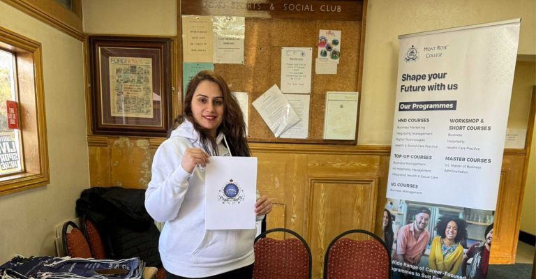 Woman representing Mont Rose College at the Lohri Community Event in Newbury Park, holding college materials beside a programme banner.
