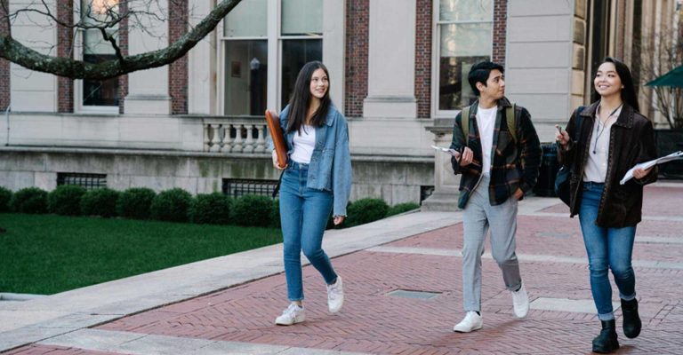 Students walking across a campus with books and backpacks, exploring higher education choices in college vs university pathways.